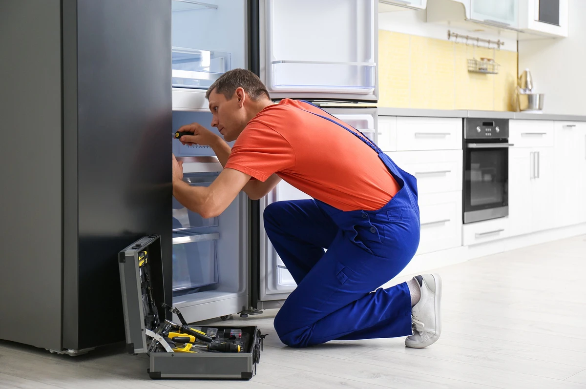 Technician with a screwdriver repairing an open refrigerator in a residential kitchen