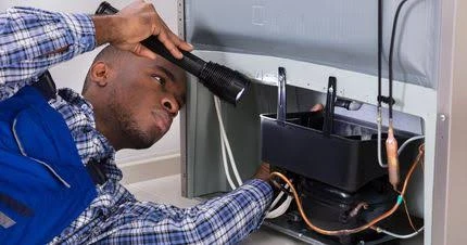 Technician using a flashlight to inspect refrigerator compressor components