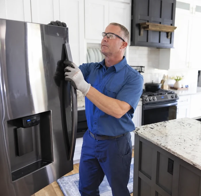 Technician wearing glasses inspecting a stainless steel refrigerator door
