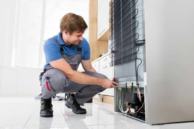 Technician examining the compressor behind a refrigerator